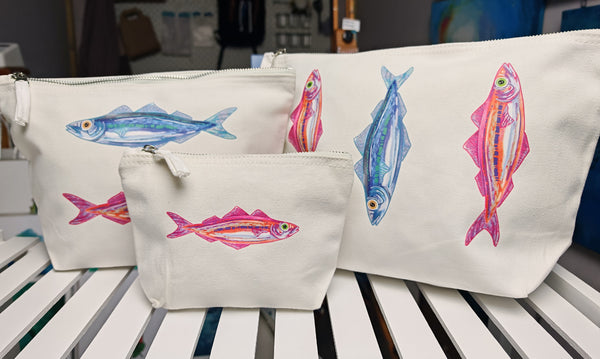 set of three, small medium and large cosmetic accessory travel bags, set together side by side featuring the designs of the sardines in pink and blue
printed onto an off white brushed cotton canvas bag with silver zip, this features a pink and orange sardine and blue and green sardine illustration by hlsdesigner and is pressed in house.