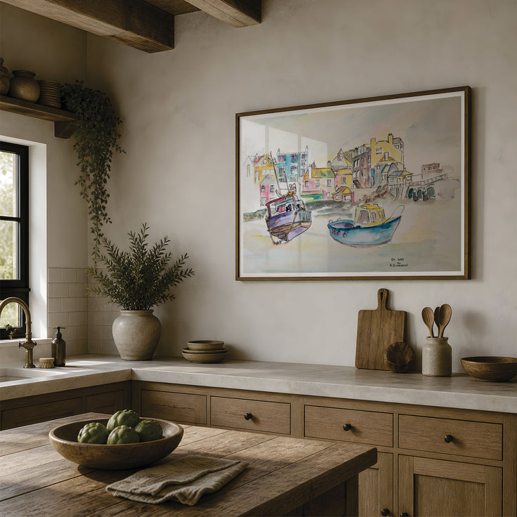 A framed watercolor painting of colorful boats and buildings hangs on a beige wall in a rustic kitchen with wooden cabinets, a stone countertop, and a wooden table in the foreground. This is a reproduction print of a watercolour painting of ST.IVES and the fishing boats moored on the sand. A beautiful representation of this popular cornwall destination boasted in colour and washes to create a contemporary feel. Originally painted by Robert Singleton and reproduced exclusively by HLSdesigner.