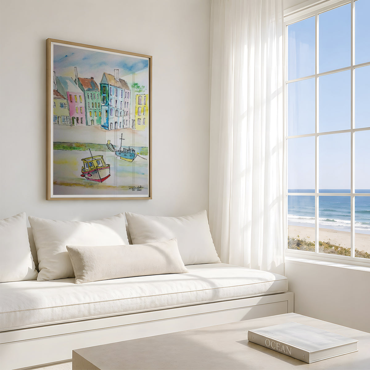 A framed colourful coastal painting hangs on a white wall above a cream daybed in a bright, modern room with a window overlooking the ocean and beach. This reproduction is of ST.VES in Cornwall, originally painted in watercolour by Robert Singleton from Cornwall. Beautifully representing a contemporary and minimal approach to the popular seaside destination. These prints are now sold only through HLSdesigner- capturing the beauty of the coast