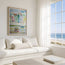 A framed colourful coastal painting hangs on a white wall above a cream daybed in a bright, modern room with a window overlooking the ocean and beach. This reproduction is of ST.VES in Cornwall, originally painted in watercolour by Robert Singleton from Cornwall. Beautifully representing a contemporary and minimal approach to the popular seaside destination. These prints are now sold only through HLSdesigner- capturing the beauty of the coast