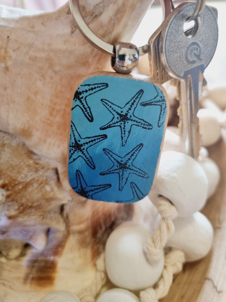 Blue keychain with starfish pattern on a beach setting, hand painted keyrings by HLSdesigner
