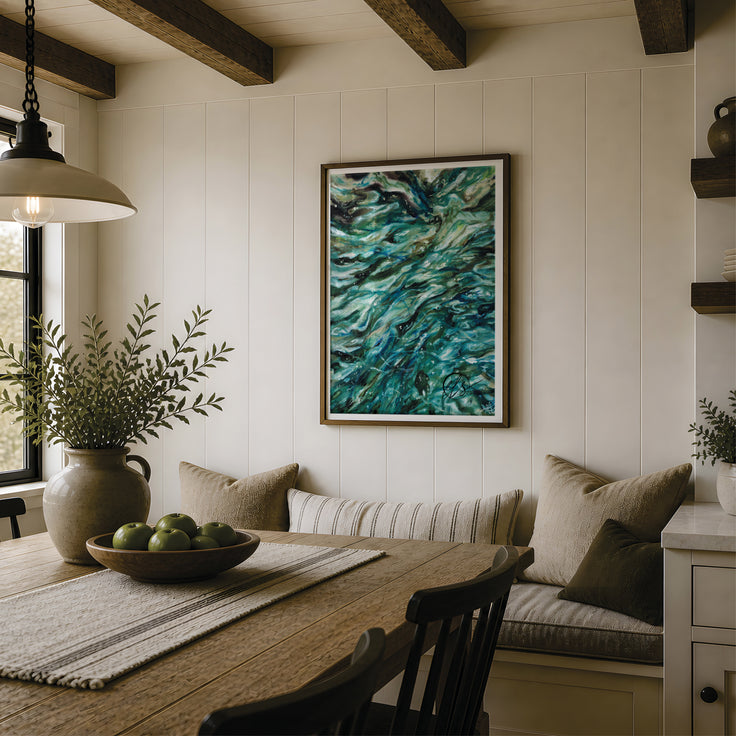A framed abstract painting with swirling teal, blue, and green brushstrokes hangs on a white panelled wall in a rustic dining room setting with a wooden table, bench, and hanging lamp. Swirling shallows. Fine art print featuring teal greens of shading and blending techniques to form a contemporary and modern abstract art piece that looks stunning in any space. Close up ocean viewpoints inspire Hannah Singleton in her artwork, designed and reproduced by Hannah at HLSdesigner