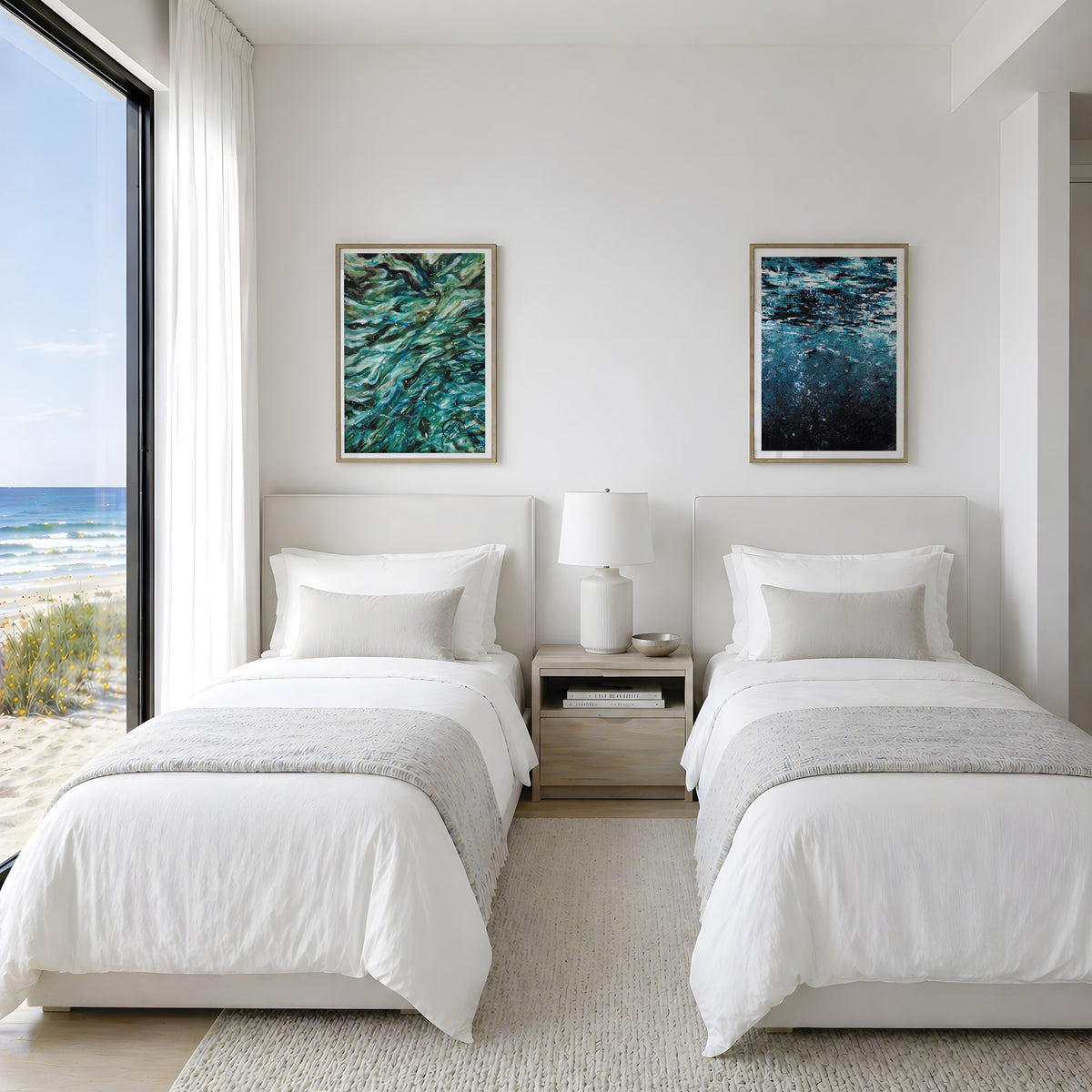 A bright, modern bedroom featuring two single beds with white bedding and gray throws, flanking a light wood nightstand. Above the beds are two framed abstract ocean-themed paintings. These paintings are reproduction fine art prints of swirling shallows - a painting inspired by shallow water reflecting in the sunlight and Shine from under - a painting depicting the depths looking up toward the reflections in the surface as the bubbles rise. Designed by HLSdesigner. Hannah Singleton contemporary ocean artist