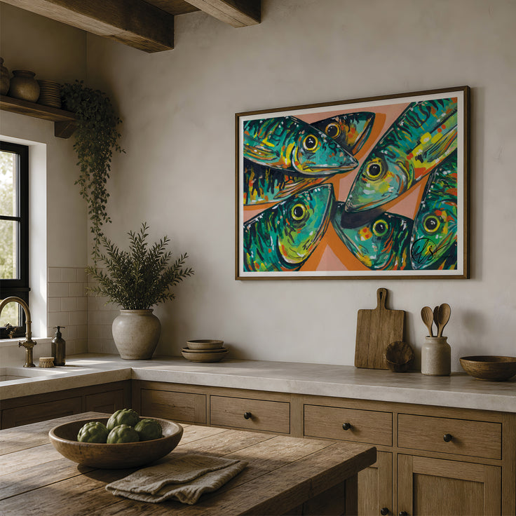 A framed colourful art print depicting four stylized green and blue mackerel fish on a peach background, hanging on a beige wall in a rustic kitchen setting. designed by Hannah Singleton fine artist at HLSdesigner, please note image of print not to print size scale. Made in Cornwall 