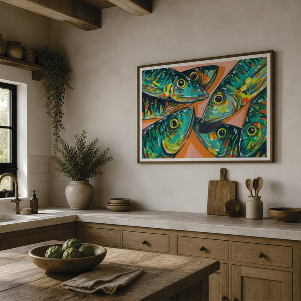 A framed colourful art print depicting four stylized green and blue mackerel fish on a peach background, hanging on a beige wall in a rustic kitchen setting. designed by Hannah Singleton fine artist at HLSdesigner, please note image of print not to print size scale. Made in Cornwall 