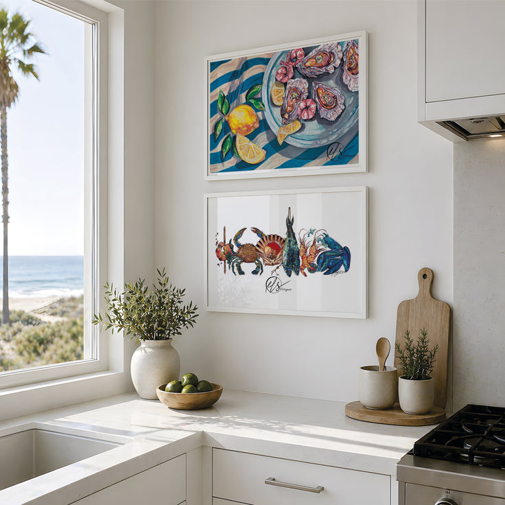 Two framed colorful paintings hanging on a white kitchen wall above a counter. The top painting shows a seafood platter of oysters with lemons and leaves on blue striped linens, and the bottom painting shows another seafood platter featuring various fish and shellfish, together making a cohesive set of art prints. Displayed in line with another on a white wall in a clean white kitchen, images are for reference only and do not display the prints to size scale. Designed painted and created by HLSdesigner