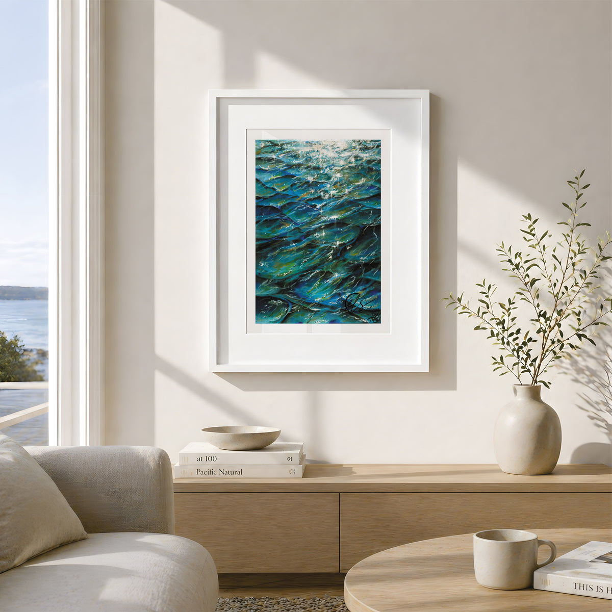 Tranquil hues - a fine art print reproduction of an original painting by HLSdesigner - Hannah Singleton fine artist and illustrator inspired by the ocean and the unique viewpoints of reflections bouncing off the sea surface and underwater. Featuring bold indigo hues and turquoise with green algae blooms throughout, white light reflect off the peaks as the waves slowly move by. Image shows positioned framed on a wall with a coastal theme throughout and an ocean view in the background