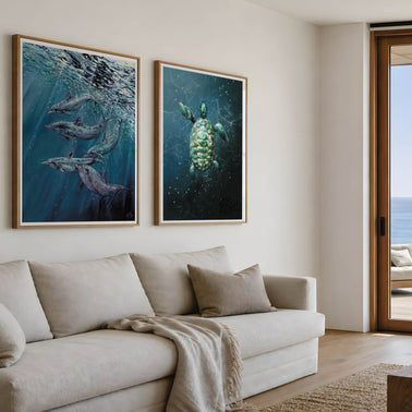 A modern coastal cream coloured reception room featuring a patio door leading to the beach outside, the perfect beach house isn’t complete without beautiful art prints framed on the wall by HLSdesigner. Featuring underwater song, a painting inspired by dolphins under the reflections of the ocean surface after jumping back in from a breach jump. Alongside this is the print of Take a breath, an illustration featuring a sea turtle at the surface of the ocean from a aerial viewpoint, watermarked by HLSdesigner