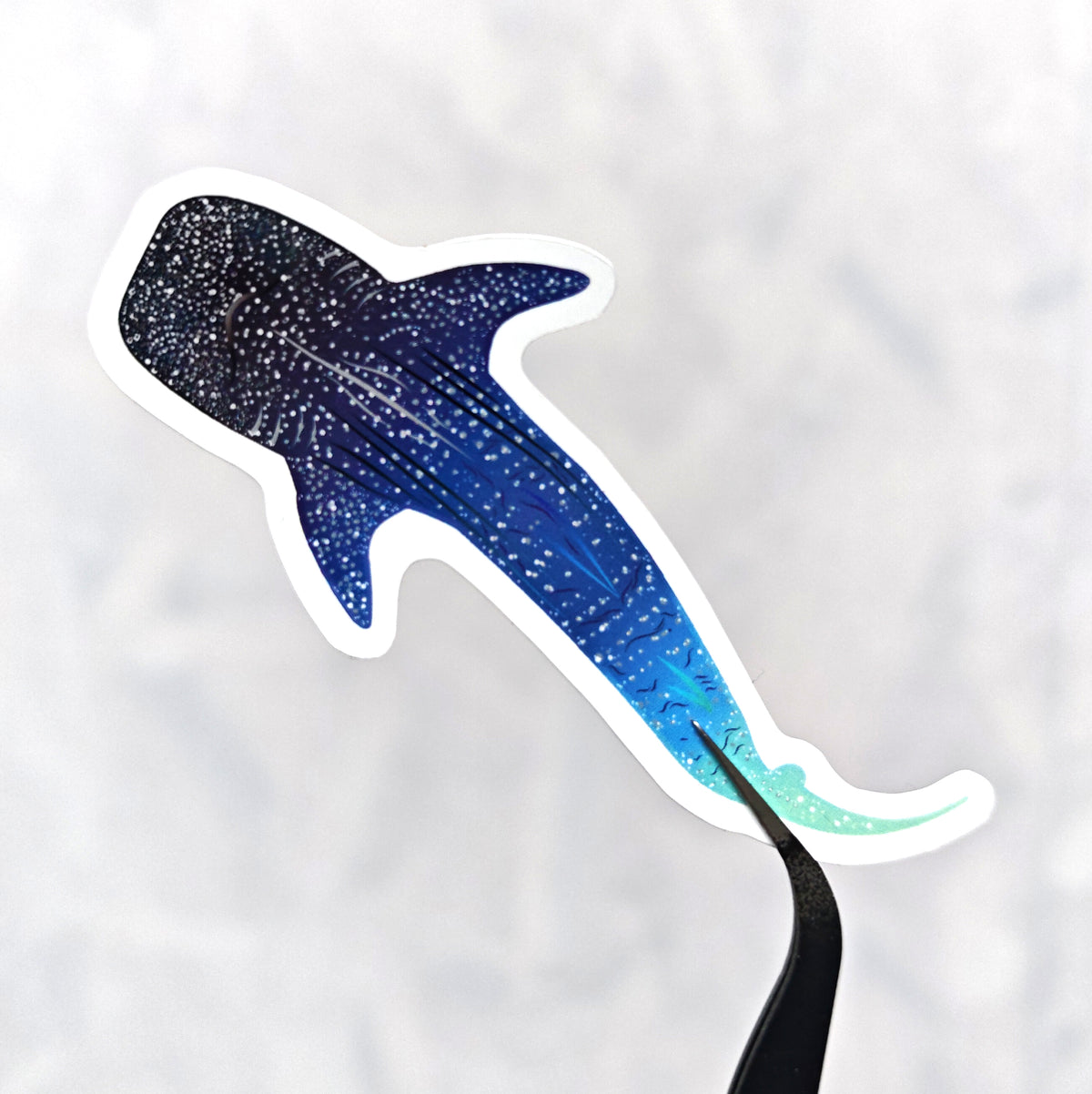 whale shark illustration inspired by constellations under the sea, merging from green to blue and black with star like spots all over, made into a beautiful die cut vinyl sticker and held with tweezers on a white background, designed by HLSdesigner